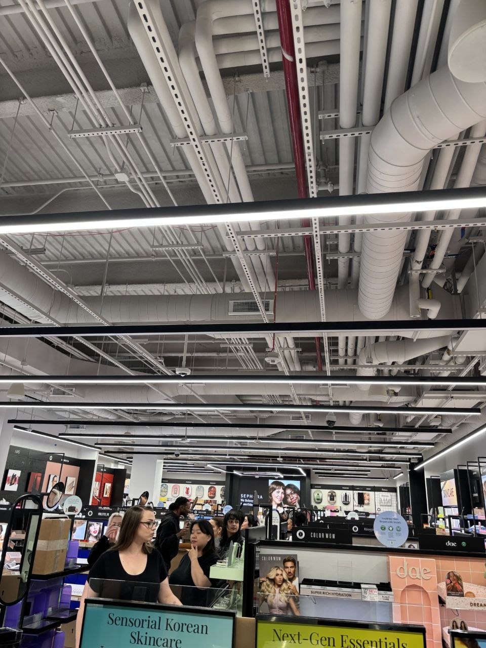 Finished Sephora retail floor with exposed black-painted ceiling, linear lighting, and overhead spiral ductwork above cosmetics displays